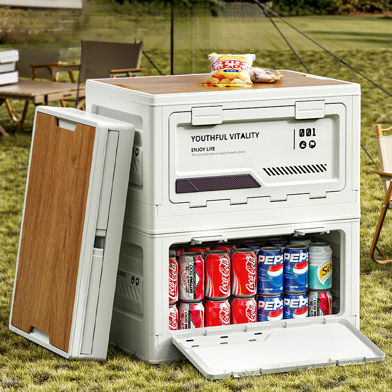 White foldable storage box (YOUTHFUL VITALITY) with front door open, storing Coca-Cola and Pepsi cans inside, wooden board top with a bag of chips, set outdoors on grass.