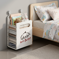 Wall-mounted foldable storage organizer in open position beside a child's bed, holding folded clothes on shelves and books, stuffed animals on top, with a cute dog 'Let's Party!' print design.