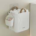 UNEDO wall-mounted foldable storage basket hung with adhesive hook, filled with rolled white towels, with side caddy holding rolled socks and small items.